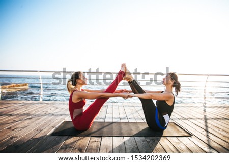 Side view of two sporty women stretching upside down while practicing pilates