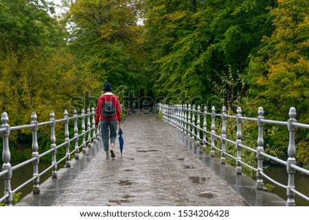 Metal railing bridge after a rainy day and woman cross the bridge with closed umbrella.