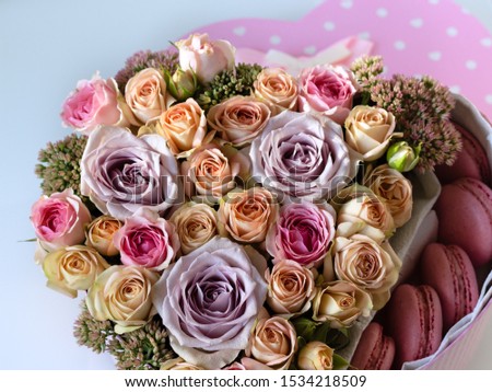 heart-shaped box with live flowers: pink and beige Bush roses, purple one-headed roses, Sedum and pink macaroni, with lid, on table close-up with blurred background as background