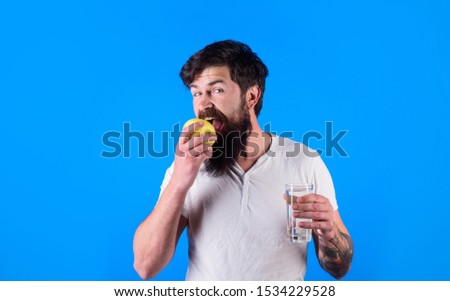 Healthy nutrition. Sport, diet, healthy lifestyle. Athletic man holds glass of water eat apple. Handsome bearded man with glass of water eat apple. Sportsman in white t-shirt holds water eating apple.