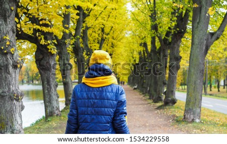 a girl in a jacket and hat walks along the autumn alley