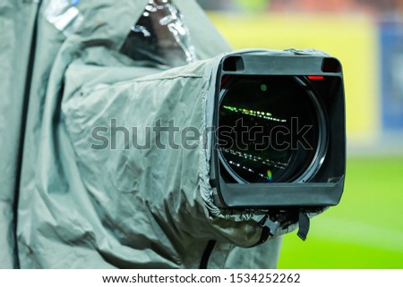 Details of a professional television camera, with rain cover, live broadcasting a soccer game.