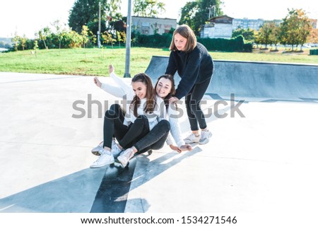 Schoolgirls teenagers girls, 3 girlfriends ride skateboard, have fun, happy have fun, play, relax after school, emotions of joy and delight of pleasure. In summer city nature. Autumn warm sweaters