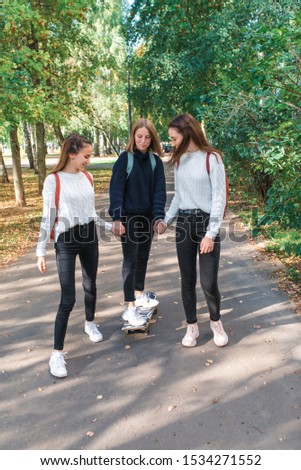 Schoolgirls teenagers girls, 3 girlfriends ride on skateboard, summer in park, background trees, autumn leaves, happy having fun playing, relaxing after school.