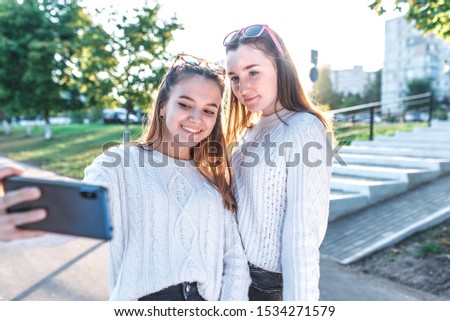 Schoolgirls teenagers girls, 2 girlfriends take pictures themselves on phone, happy smiling have fun, record video, video call, have fun in city in summer, happy play, relax after school