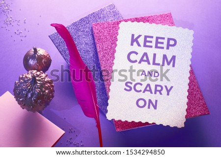 Creative purple and pink Halloween background with levitating pink pin quill, stack of glittering paper and decorative pumpkins painted metallic pink. Copy-space, on the silver paper.