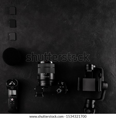 Work space videographer with laptop, digital camera, memory card, action camera, drone, remote controller, phone and camera accessory. Top view on black table background.