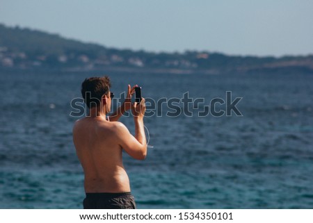 Person with headphones taking a picture of the sea with his cell phone