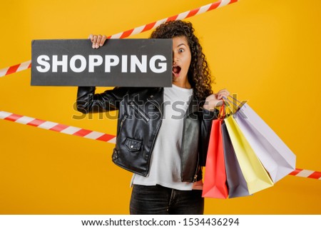 black woman with shopping sign and colorful shopping bags isolated over yellow with signal tape