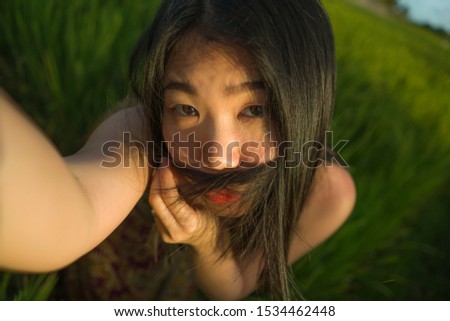 young happy and beautiful Asian woman taking selfie photo outdoors . cheerful Korean girl in Summer dress taking self portrait at green field enjoying holiday travel in tourism concept