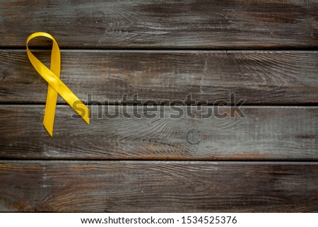 Disease control concept. Yellow ribbon on dark wooden background top view space for text