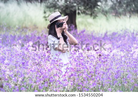 Photographer tourist make photo on camera. Girl in hat with dresses travels in Romantic trip to beautiful purple flower field.