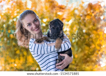 Portrait. Happy girl holding a German shepherd puppy and smiling. Buying and acquiring a dog, the joy of meeting an animal. Funny watchdog. On a blurred yellow autumn background. copy space