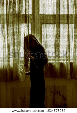 Girl dressed as witch, standing behind the curtain, scary scene. Halloween concept