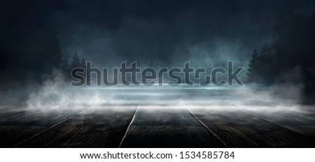 Abstract dark empty scene. Abstract night landscape. Neon blue light, tree silhouettes, wooden table, reflection in the water,  Misty forest, dark, smoke, smog. Night view.
