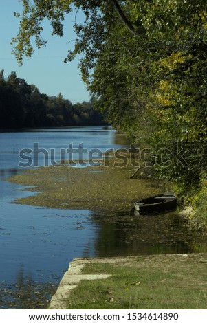 A small abandoned boat at the end of the quay which has drifted away from it mooring. The blue sky and blue river of The Dordogne are in the foreground and background.