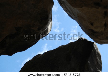 Rock formation of three stones. Megalith rocks standing together. Inside a canyon, camera facing upwards to the bright sky. Daylight. Inside a cave or sandstone canyon.