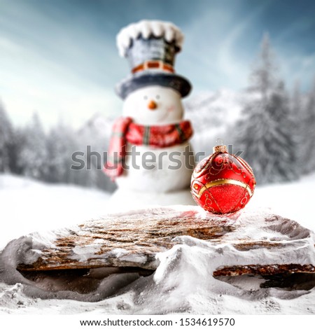 Snowy winter sunshine landscape with wooden board top for products and decorations. Blurred snowman background.