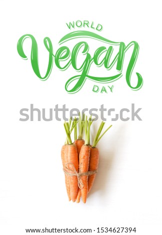 Bunch of fresh carrotson white wooden background. Hand sketched World Vegan day text.