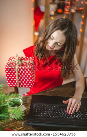 A beautiful woman in a red dress receives a gift via the Internet for the New year. Online shopping for Christmas holidays.