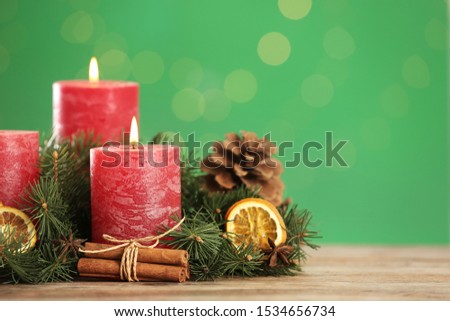 Beautiful Christmas composition with burning candles on table against green background. Space for text