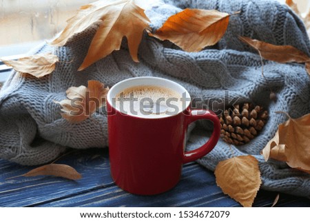 Cup of hot drink, sweater and autumn leaves on windowsill. Cozy atmosphere