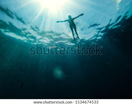 Underwater photo of woman floating in the sea and rays of light piercing through Royalty-Free Stock Photo #1534674533