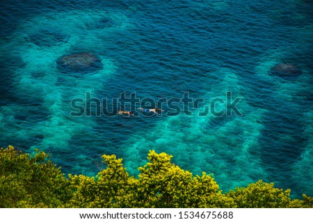Aerial view of couple snorkeling in turquoise waters with coral background in Koh Tao Island, Thailand. Snorkeling tour in exotic scenarios. Concept of couples goal and summer vibes.