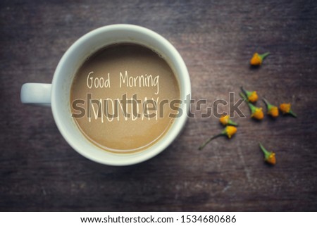 Cup of coffee top view. Morning white coffee with greeting text on it - Good Morning Monday, and yellow little flowers arrangement on natural wooden table background.