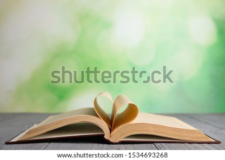 Open book on grey wooden table against blurred green background. Space for text