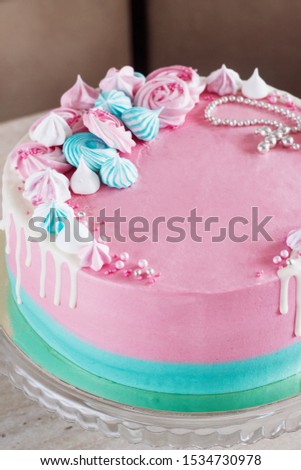 Pink cake for the baptism of a girl on a light background with meringues and a cross.