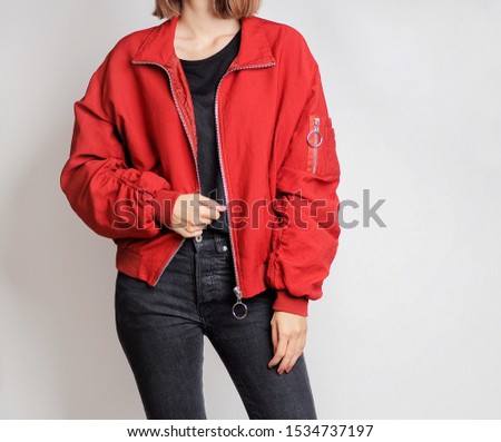 Young woman wearing red bomber jacket, black sweater and high-waisted jeans isolated on white background. Copy space