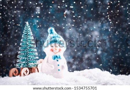 Merry Christmas and happy New Year composition with copy space. Little snowman carries Christmas tree from fairy forest to home. Winter festive background