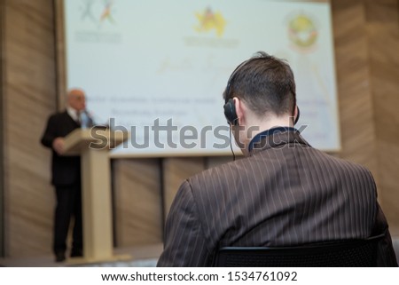 Man with headset at the conference . The audience wearing head phone for online translation . Unrecognizable people using in ear headphones for translation during event