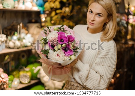 Girl holding a christmas composition with purple pink and white peony roses decorated with green leaves in the blurred background of flower shop