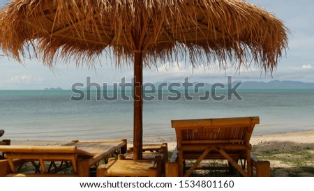 Sunshades on sea background. Sun umbrellas from straw and palm trees on ocean and sky background in Thailand. Relax, Travel vacation holiday resort concept