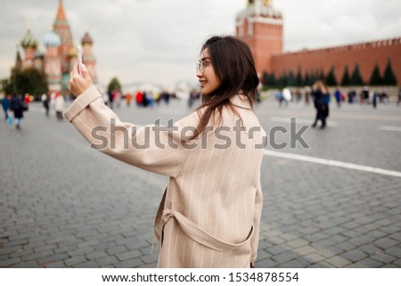 A beautiful tourist of Asian appearance takes a selfie standing in the middle of red square