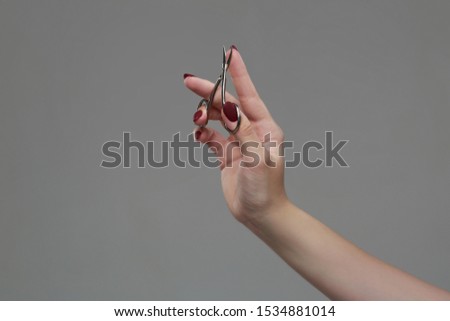 Female hand with a beautiful neat manicure holds nail scissors Isolated on a gray background.