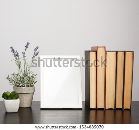 empty white photo frame, stack of books and a pot of growing lavender on a black table, workplace 
