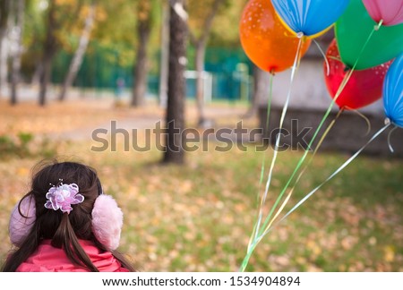 Autumn day. A girl holds balloons filled with helium. In the frame, the girl's head in headphones with a bow. Defocus on the balls. Horizontal frame. Color image