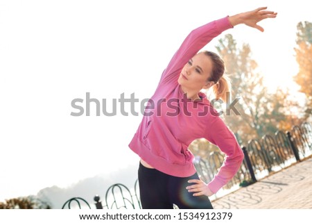 Young woman maintaining healthy lifestyle doing warm up outdoors autumn season bending aside stretching back breathing concentrated