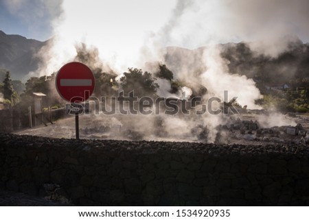 Sunny morning in a city in a valley, with many natural hot springs, creating a steam, highlighted by the sunshine. No entry traffic sign in the foreground. Furnas, Sao Miguel, Azores Islands, Portugal