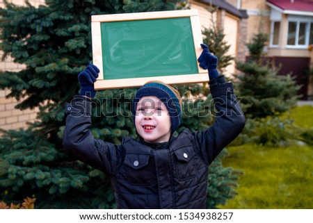 The boy smiles. A child in warm autumn clothes holds a sign on his head with the inscription chalk Autumn sale. The beginning of the sales season.