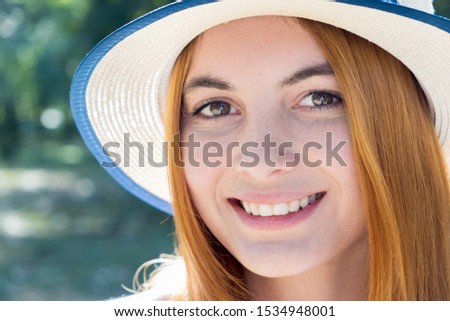 Portrait of gorgeous smiling teenage girl in yellow hat and with red hair outdoors on sunny summer day.