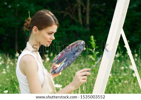 young woman on nature an easel paints with paints