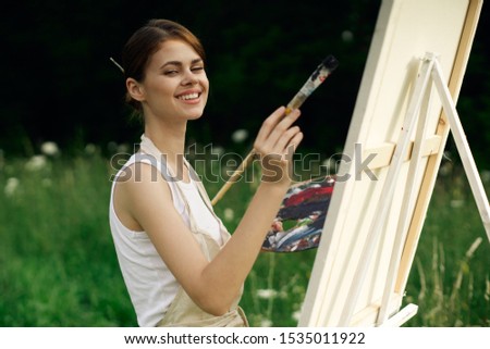 young woman looking at the camera an easel with paints