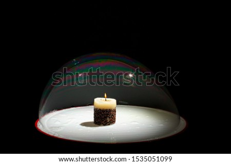 A burning candle inside a large soap bubble on a black background. Magical performance. Magic tricks. Rainbow soap bubble. Colored large balls. Holiday. Christmas. Soap bubbles show. Entertainment.