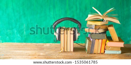 audio book concept with opened book, row of books and headphones, panorama format on grungy background, good copy space