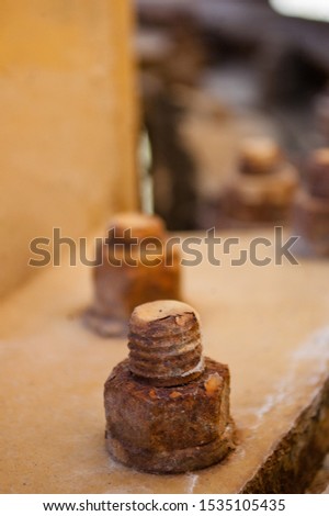 Several large rusty bolts of an abandoned road paver with a blurry background.