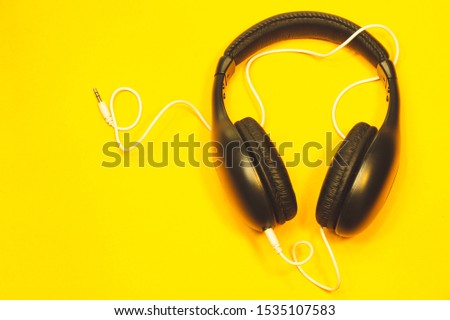 Black headphones with white cable on a yellow background. modern earphones